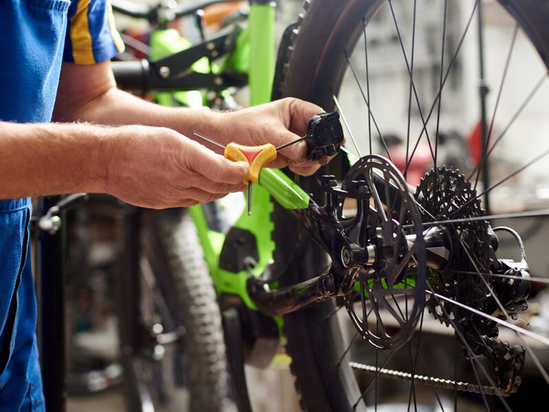 Cropped shot of male mechanic making service in bicycle repair shop, repairing modern bike brakes using special tool, wearing protective workwear
